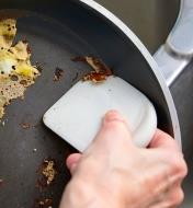 Using the rounded edge of a pan scraper to scrape food from the edge of a frying pan