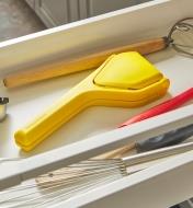 A folded lemon & lime juicer in a drawer with various kitchen tools