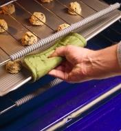 Oven shelf guards on the edges of two oven racks as a sheet of cookies is placed between