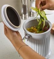 A woman puts vegetable peels into a porcelain compost pail