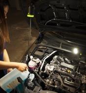 Refilling a car’s windshield-washer fluid, with two rechargeable clip lights mounted under the hood