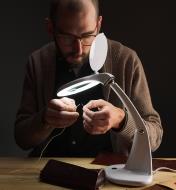 A man uses an LED tabletop magnifying lamp to help thread a needle