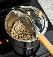 The lid of the stainless-steel Whirley-Pop popcorn popper opened to show the stirring device at work inside the pot