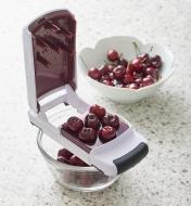 A multi-cherry pitter with six cherries on top of a bowl