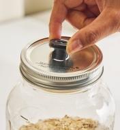 Inserting an Airtender stopper into a hole cut in the lid of a Mason jar