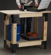 A man with a drill and case of accessories stands at a table made with a utility table hardware kit