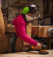 A child sanding wood while wearing hearing protectors, safety glasses and a dust mask