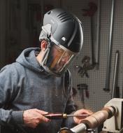 A person wearing a full-face shield while turning wood on a lathe