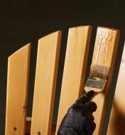 Personne applicant à l'aide d'un pinceau une couche d'huile de protection anti-UV Osmo sur une chaise Adirondack en bois