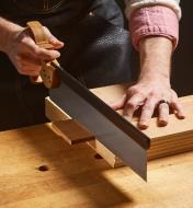Using a carcass saw to cut a board resting on a block of wood