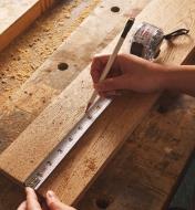 Using a washable tape measure and a pencil to mark a line on a board on a sawdust-covered workbench