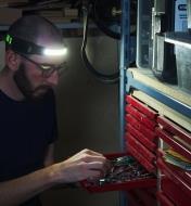 A man uses the COB headlamp’s LED strip to help select a wrench from a drawer in a darkened workshop