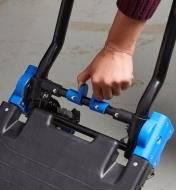 A person squeezes the release clip on the dual hand truck and moving cart