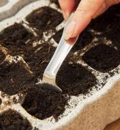 Using a potting tool to level soil in a seed starter