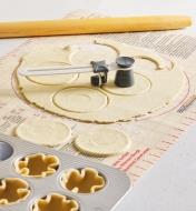 A pastry cutter cutting small dough circles next to a tart tin with dough