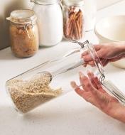 Using a long-handled measuring scoop to get oats from the bottom of a long glass container