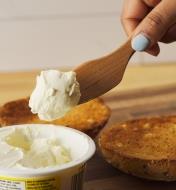 Personne s’apprêtant à étendre du fromage à la crème à l’aide d’un couteau à tartiner en érable