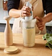 Personne réduisant en purée les ingrédients d'un lait végétal dans le filtre d'un pressoir placé à côté d'autres accessoires et d'ingrédients