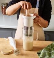 Holding a plastic filter above a glass pitcher and pressing down with a pestle