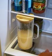 A glass pitcher, half-full of oat milk, being stored in a refrigerator