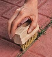 Using a weed brush to clean the cracks between patio stones