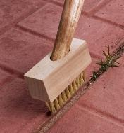 Weed brush with a handle attached cleaning the cracks between patio stones