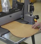 A curved piece of wood resting on an infeed/outfeed table and being fed into a 19-38 drum sander