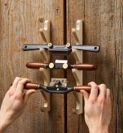 A man places a Veritas spokeshave below another spokeshave and a Chair Devil on a spokeshave rack