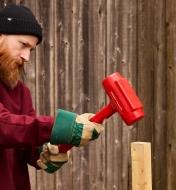 A man uses a dead-blow sledgehammer to pound a post into the ground