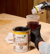 Preparing a batch of Osmo 2K wood oil by adding hardener to a mixing cup containing oil