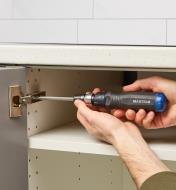 Using a 10-in-1 ratcheting screwdriver to adjust a European-style cabinet hinge
