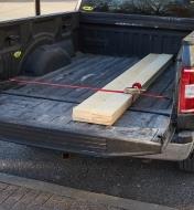 A Quickloader auto-retract ratchet strap being used to secure lumber in the bed of a pickup truck