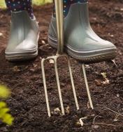 A child wearing a rubber boot pushes the children’s digging fork into soil