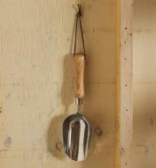 A stainless-steel scoop with a wood handle and leather loop hangs on a hook