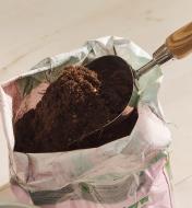 Using a stainless-steel scoop to dig soil out of a bag