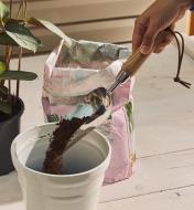 Using a stainless-steel scoop to pour soil into a pot