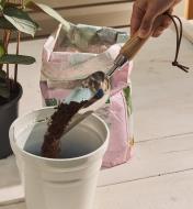 Using a 1 cup stainless-steel scoop to pour soil into a pot