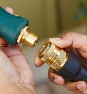 A gardener holds a nozzle with a male tool adapter in one hand and a hose end with a female coupler in the other