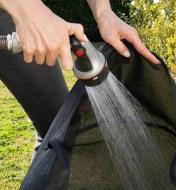 A gardener uses a hose to rinse the 10 gallon mesh fabric pot