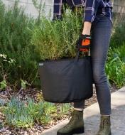 A gardener carries the 10 gallon mesh fabric pot with plants growing in it