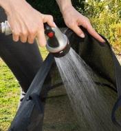A gardener rinses the 25 gallon mesh fabric pot with a hose