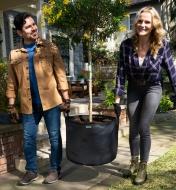 Two gardeners carry the 25 gallon mesh fabric pot with a small tree planted in it