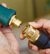 A gardener holds a nozzle with a male tool adapter in one hand and a hose end with a female quick connect in the other
