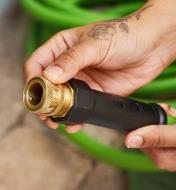 A gardener holds the end of a hose with a hose-end quick coupler attached 