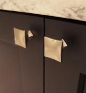 Two square golden nickel knobs mounted to cupboard doors