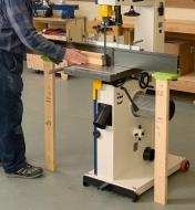 A bandsaw with an extended fence and an infeed and outfeed support and a board holding up each