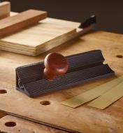 A Veritas Shooting Sander sits on a workbench beside two strips of sandpaper