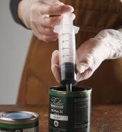 A woodworker uses the syringe to extract a small amount of wood finish from a can