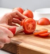 Using the serrated paring knife to slice into a tomato on a cutting board