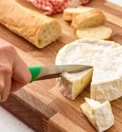 Using the straight paring knife to cut a piece of brie cheese on a cutting board next to a baguette